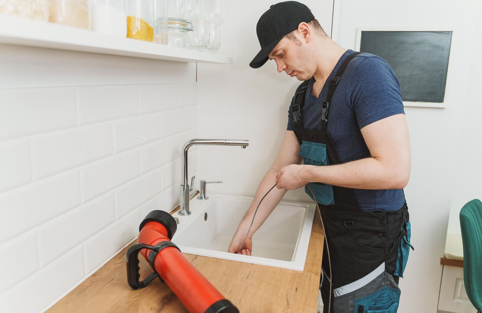 A plumber uses a drain snake to clear a clog in a kitchen sink